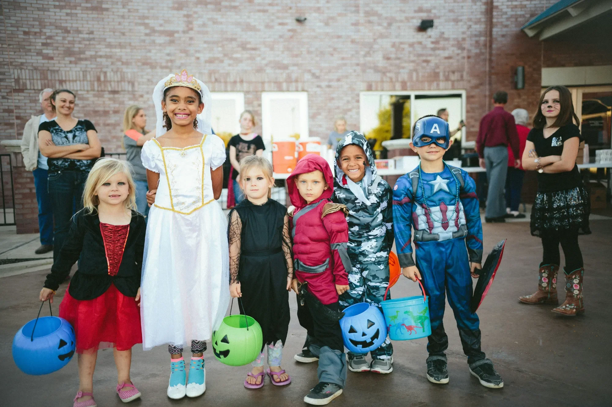Sechs Kinder in Kostümen halten Halloween-Eimer auf einer Feier.