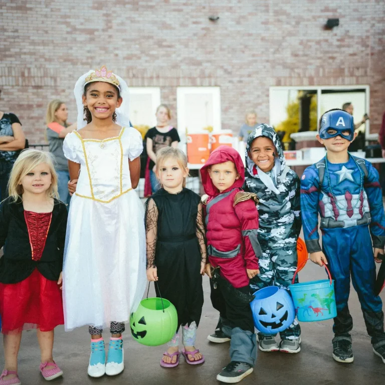 Sechs Kinder in Kostümen, die Süßigkeiten sammeln, lächeln vor einer Kulisse.