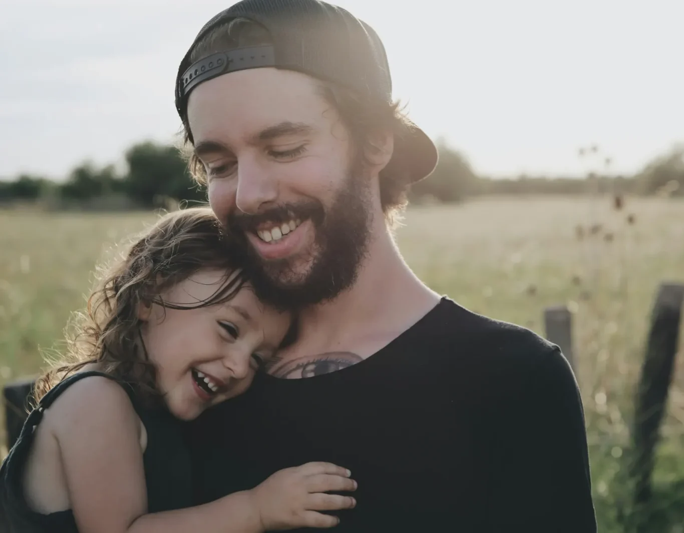 Junger Vater umarmt lächelnd sein Kind in einem Sonnenschein-Feld.