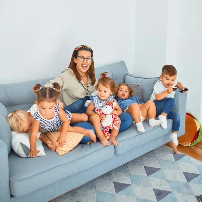 Eine Frau sitzt mit fünf Kindern auf einem hellblauen Sofa, alle lächeln und spielen.