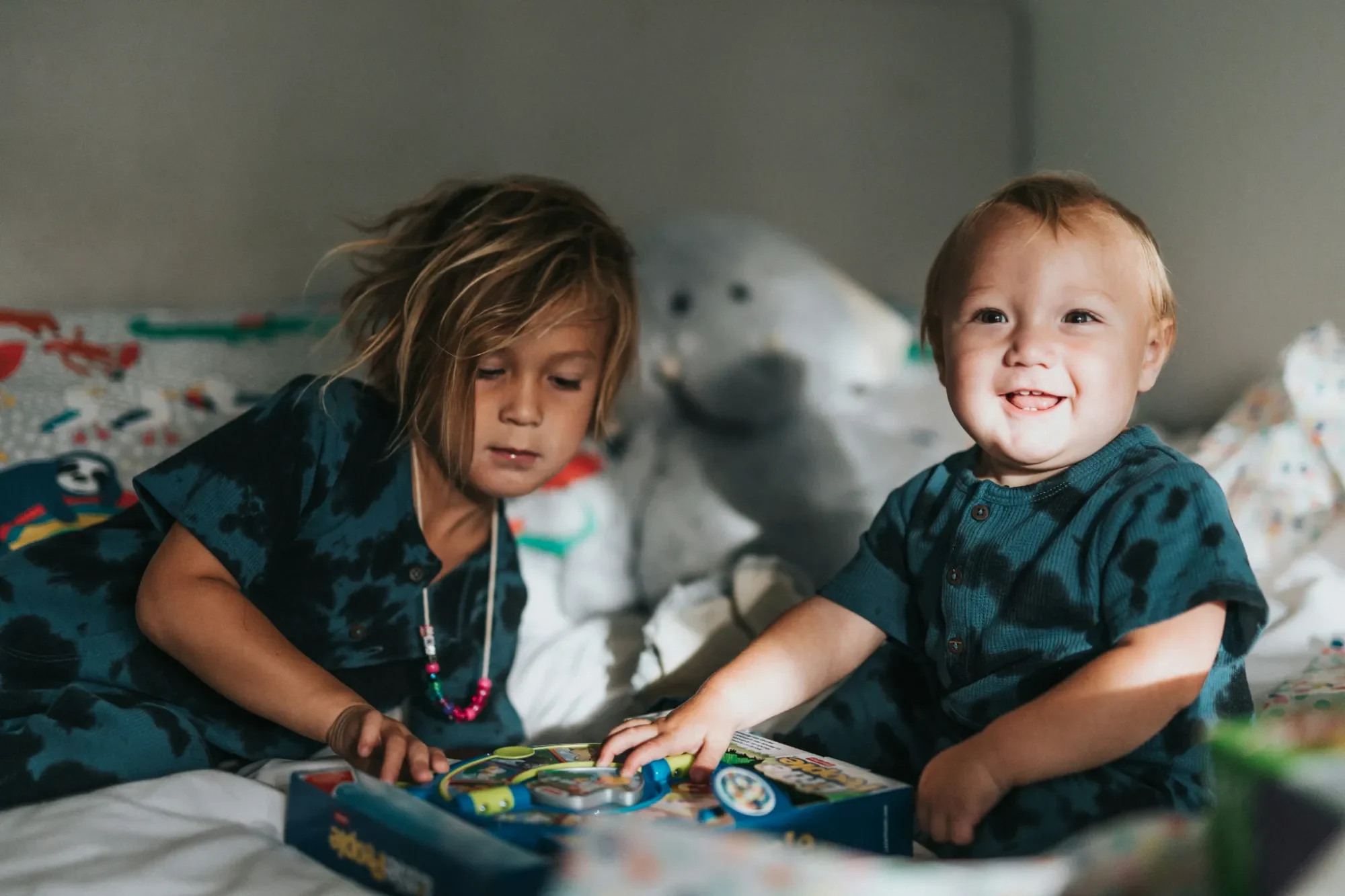 Zwei Kinder sitzen auf einem Bett und spielen mit bunten Spielzeug.