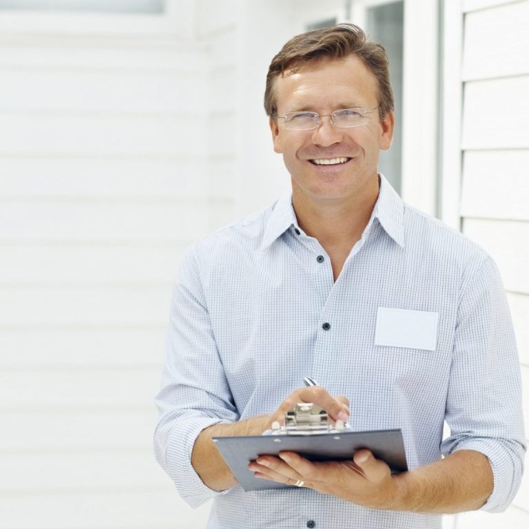 Lächelnder Mann hält ein Clipboard, trägt eine Brille, in heller Umgebung.